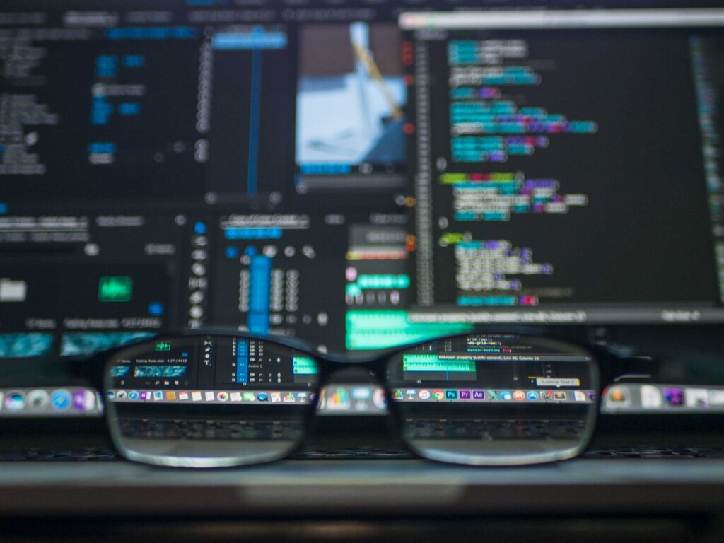 código escrito em computador ao fundo com óculos em destaque